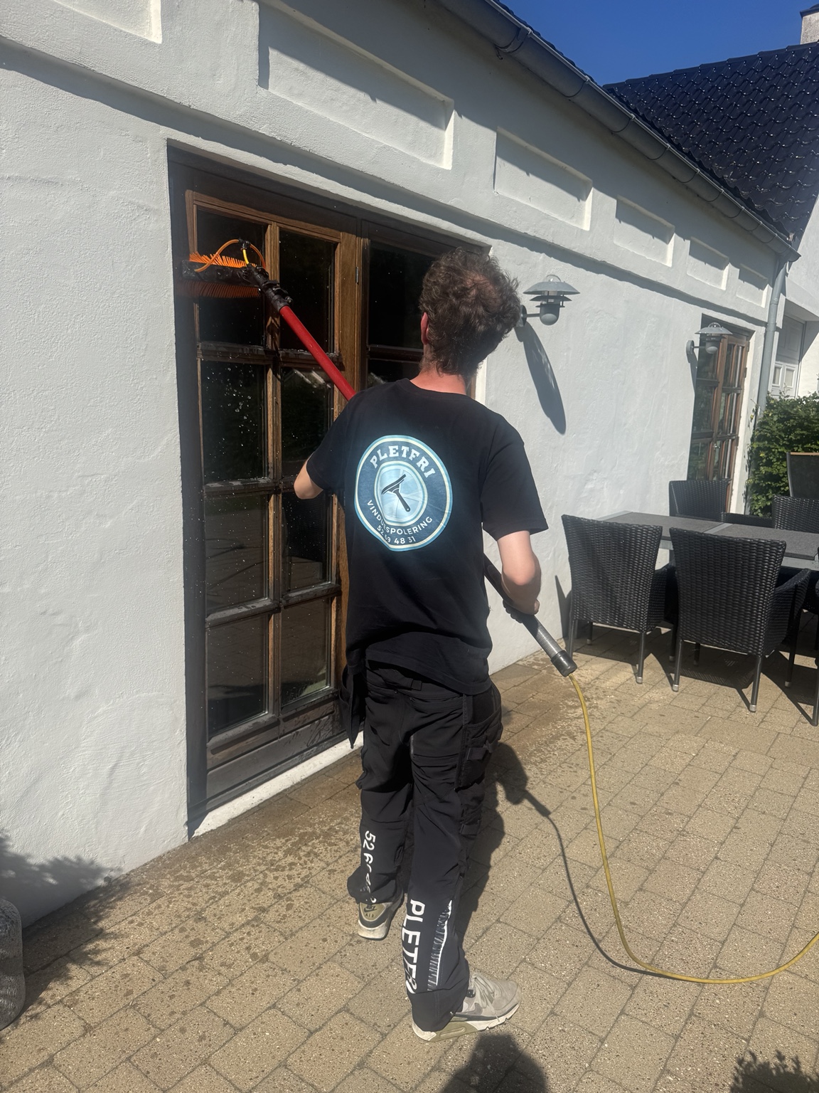 Medarbejder fra Pletfri Vinduespolering arbejder med rentvandsanlæg ved en lys villa